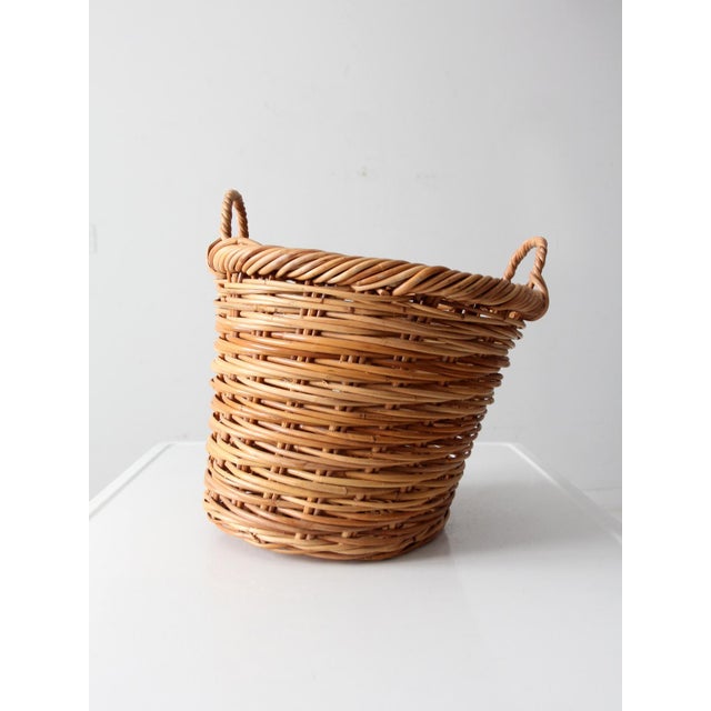 Vintage handwoven wicker basket with softly twisted side handles and a warm honey-toned patina. The organic weave and...