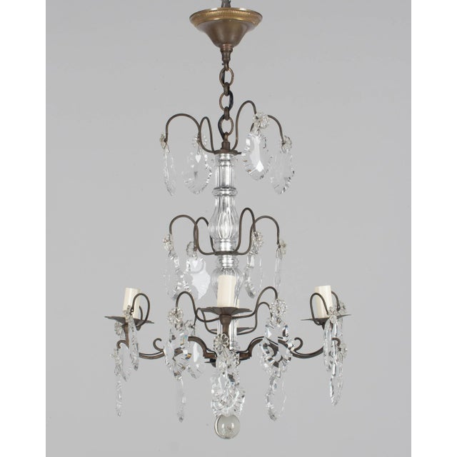 A French Louis XV style four-light crystal chandelier. Brass frame with dark patina. Crystal pendalogues with rosettes and...