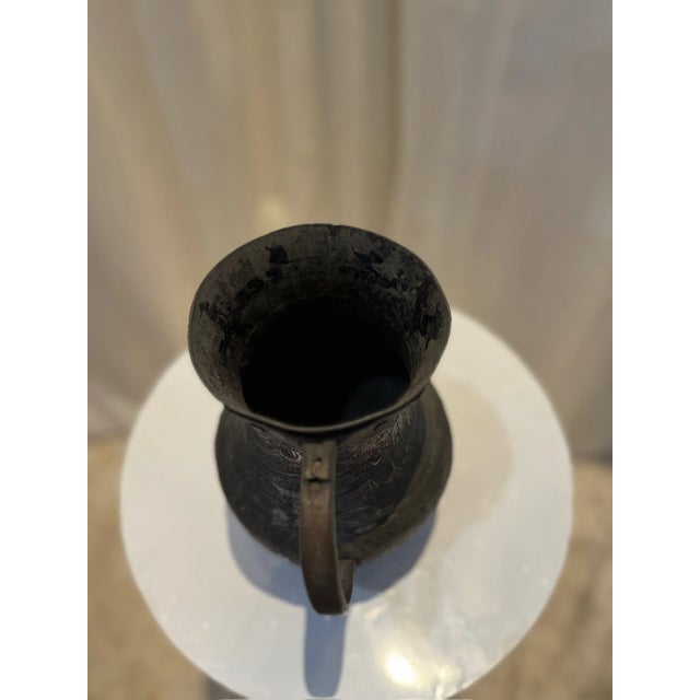 This stunning antique Middle Eastern copper pitcher is a true testament to the artistry and craftsmanship of its time....