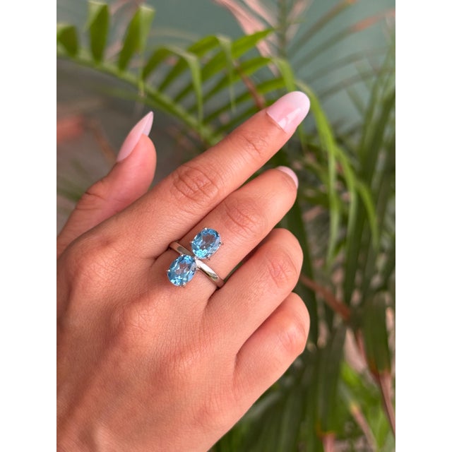 This exquisite ring is beautifully crafted in 925 Sterling Silver, showcasing two oval Blue Topaz gemstones in a refined...