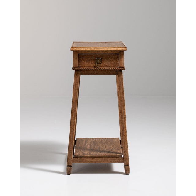 Slender oak pedestal side table in Warm Honey Oak. Its warm honey oak finish sets off single drawer, lower shelf, turned...