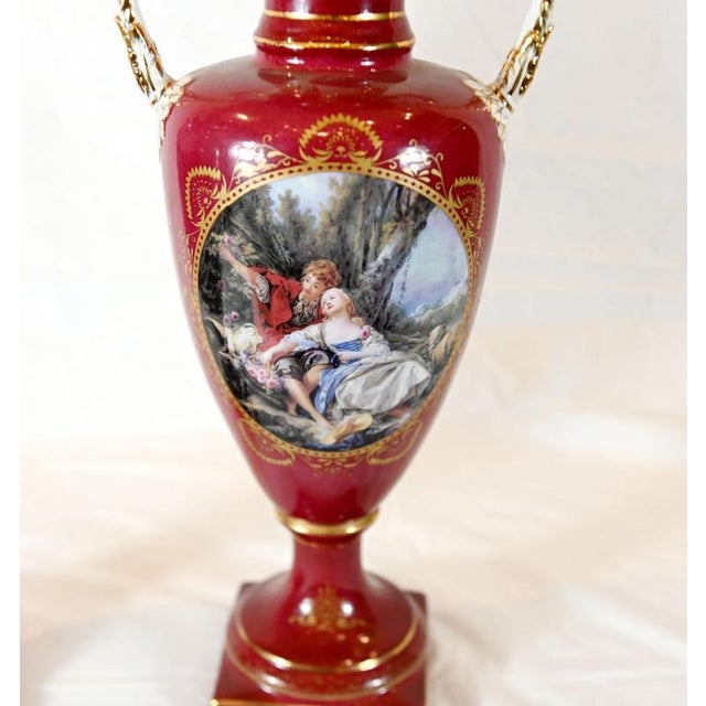 A fine pair of French Sèvres-style porcelain urns dating to circa 1880 Each urn features a rich ruby-red ground...