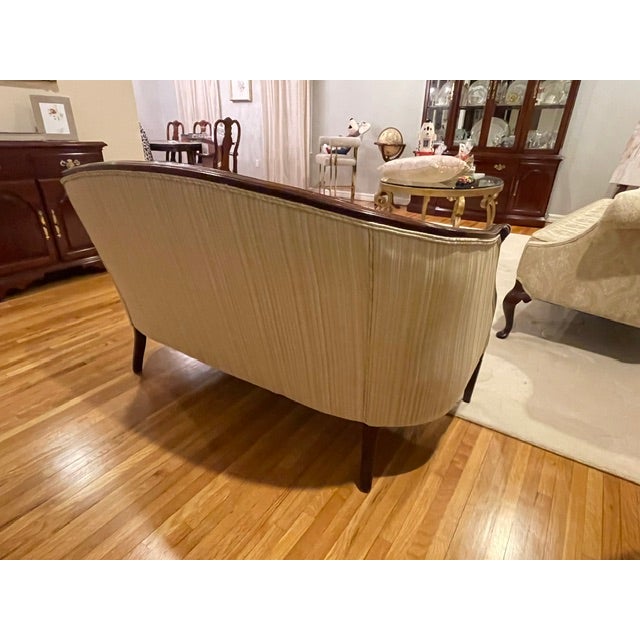 An elegant mid-century Sheraton Revival barrel-back settee featuring a gracefully curved frame and an exposed top crest...