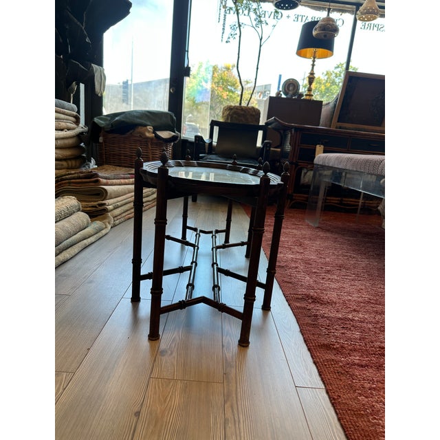 Vintage accent table featuring a scalloped, decorative brass top framed by rich, warm-toned, bamboo style wood. The table...