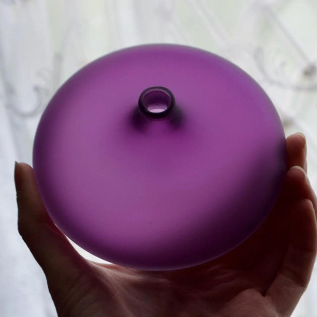 Charming signed studio art glass bud vase by Nick Kekic, featuring a compact sculptural form in a rich purple tone. The...
