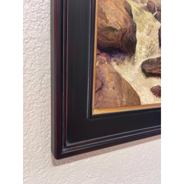 The painting depicts a dynamic river rushing through a rocky landscape, with water cascading energetically over smooth...