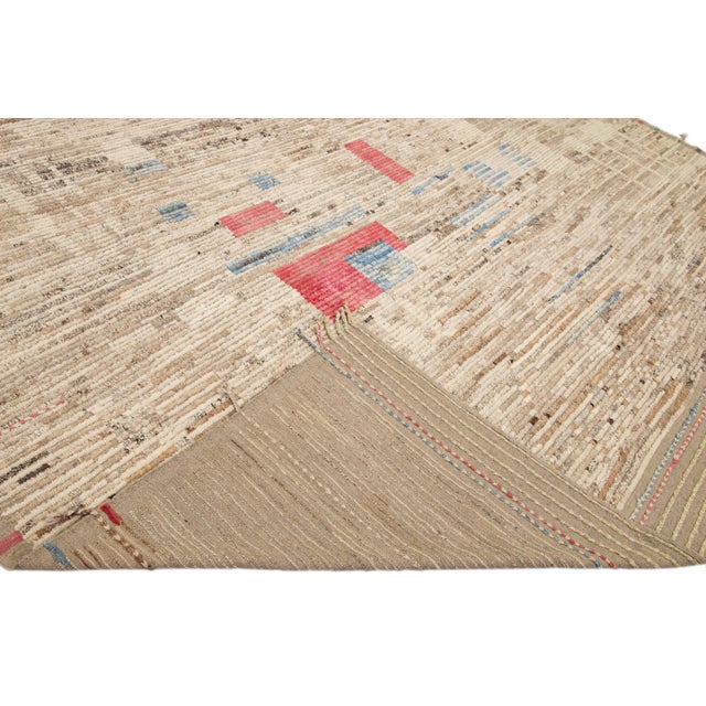 Beautiful Moroccan style handmade wool rug with a beige field. This Modern rug has brown, red, and blue accents featuring...