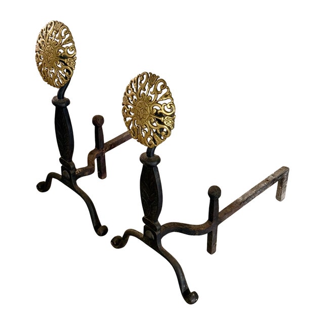 A vintage pair of Virginia Metalcrafters brass and iron andirons, featuring floral rosette medallions, vine‑incised iron...