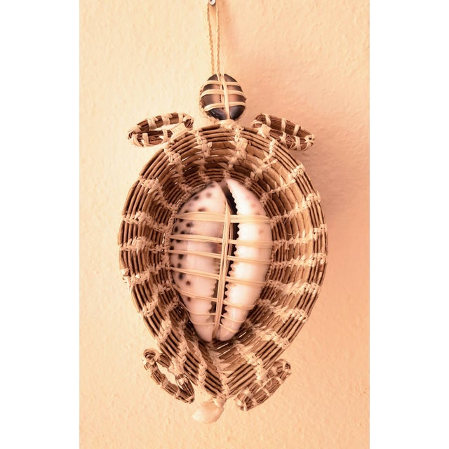 An exquisite handwoven turtle figurine, featuring a stunning tiger leopard cowrie shell at its center. This beautiful...