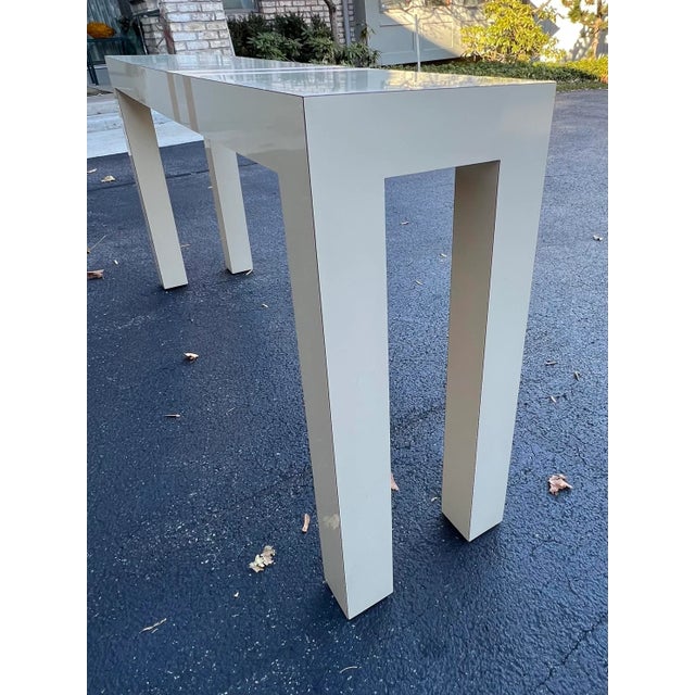 A custom parsons style lacquered laminate console / sofa table. Two parallel metal gold finish ribbons lay vertical on the...