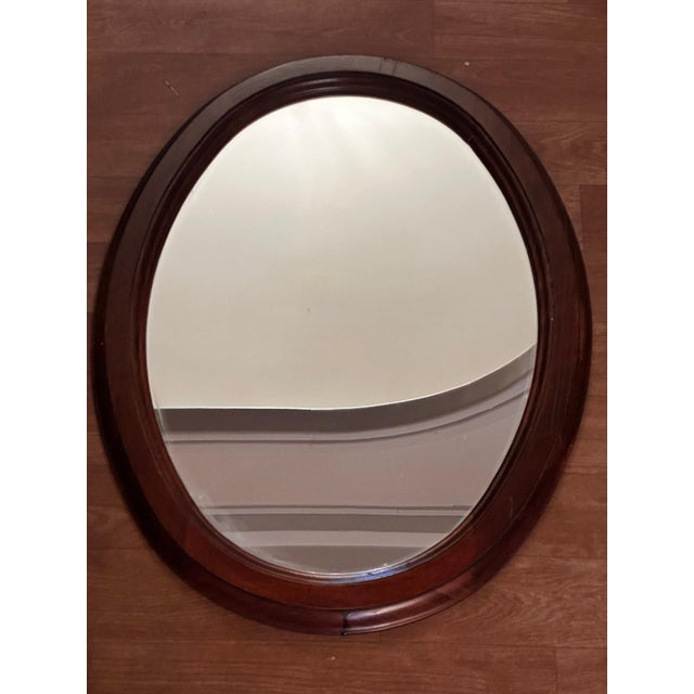 Vintage oval wall mirror, framed in stained wood with clean, elegant lines. The frame features an interior molding that...