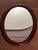 Vintage oval wall mirror, framed in stained wood with clean, elegant lines. The frame features an interior molding that...