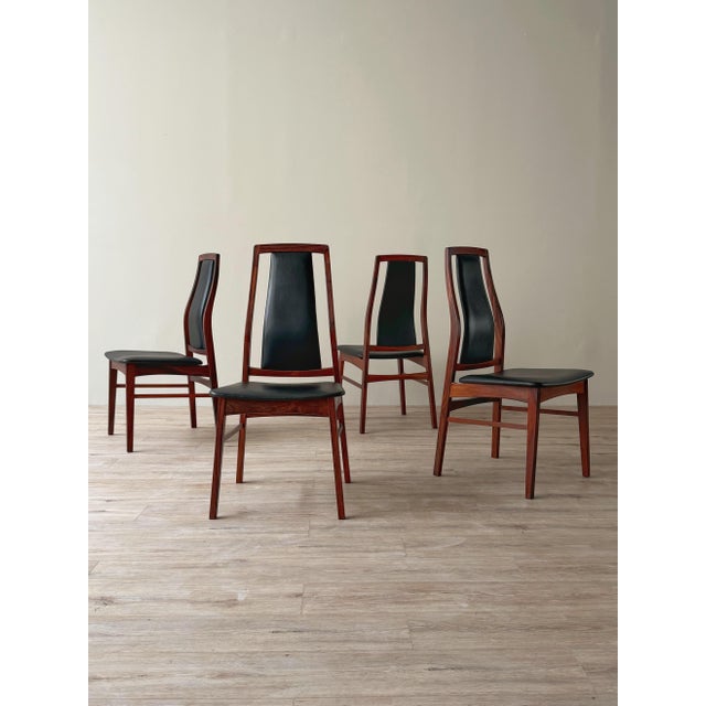 Set of four dining chairs with figured rosewood frames and black vinyl upholstered seats and backs. Each chair features a...