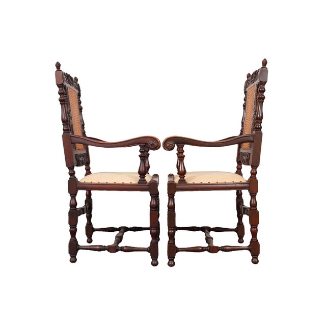 A pair of ornately carved Jacobean style armchairs. Back splats are double caned and topped with scrolled acanthus leaves...