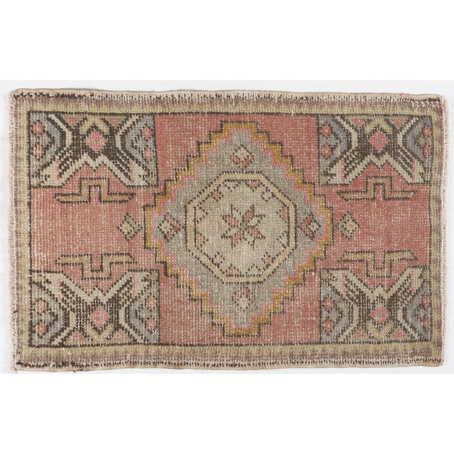 A vintage Turkish handwoven door mat rug featuring a bold geometric medallion and tribal motifs. Softly faded blush, sand,...