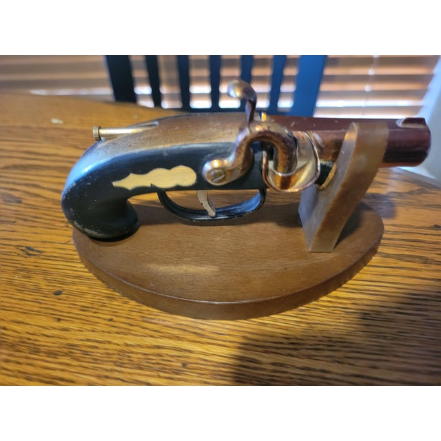 Vintage mid-century pistol-shaped table lighter mounted on a custom wooden display stand, resembling a 19th-century...