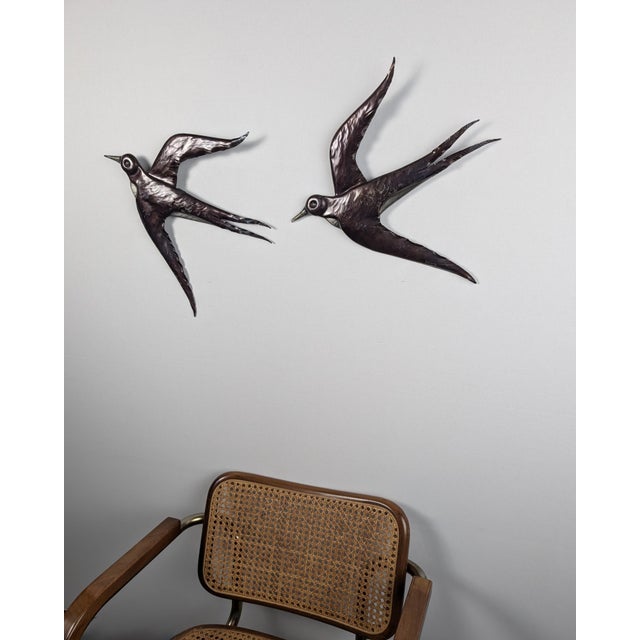 A pair of metal wall sculptures, designed in the shape of swallows in flight. The surface has a patinated, glossy metallic...