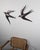 A pair of metal wall sculptures, designed in the shape of swallows in flight. The surface has a patinated, glossy metallic...