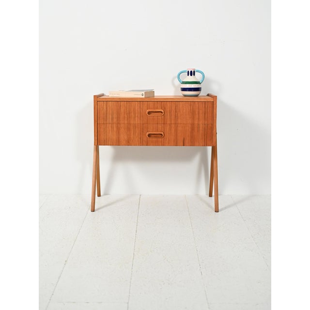 Scandinavian teak bedside table from the 1960s with two drawers, recessed oval handles, and a slender frame on slanted...