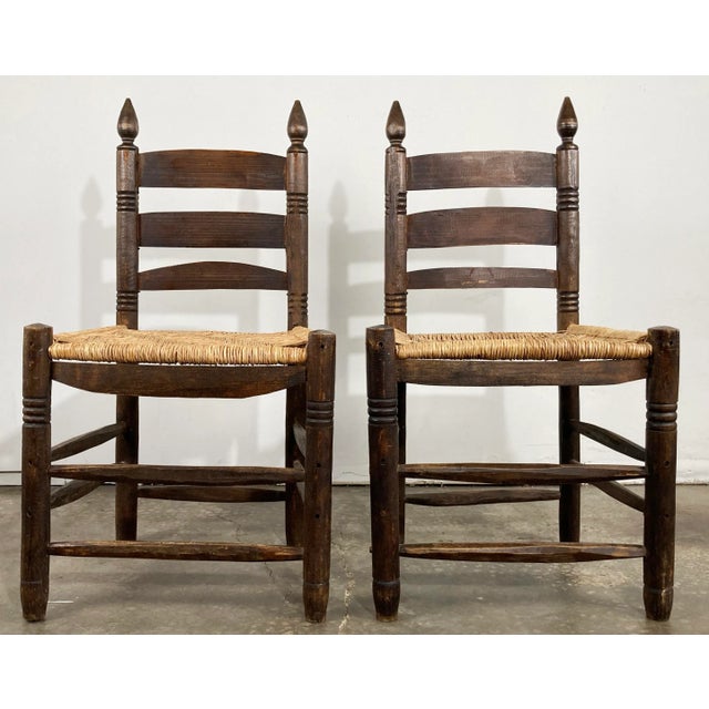 Pair of primitive handmade ladderback chairs featuring woven seats. Wonderful turned wood details to frames. Four legs...
