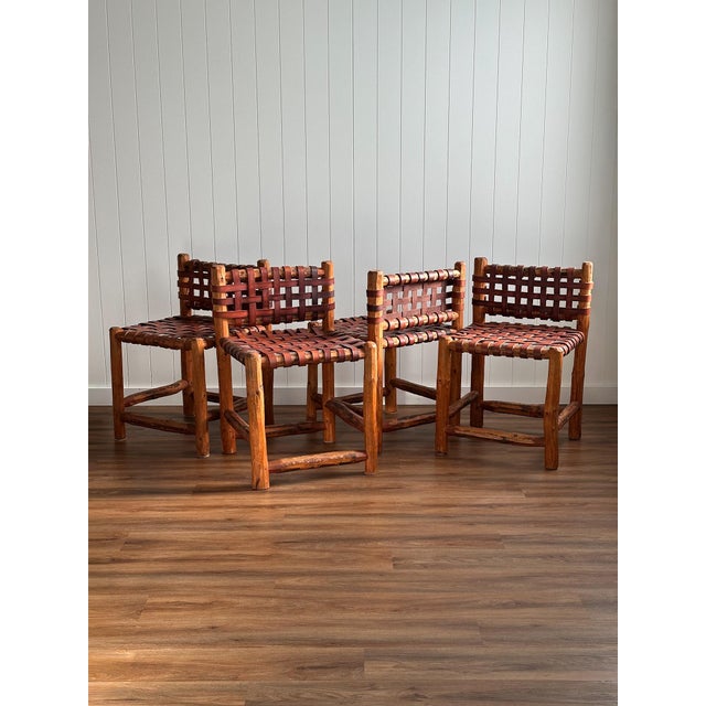 A set of four dining chairs crafted in the 1940s, constructed from solid wood with woven leather strap seats and backs....