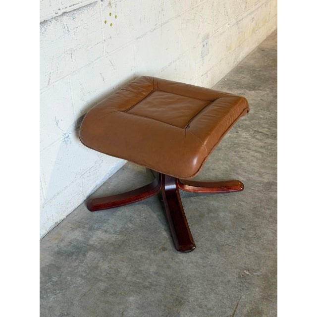 This vintage tan leather ottoman features a sculptural wooden base with sweeping arched legs. The plush cushioned top...