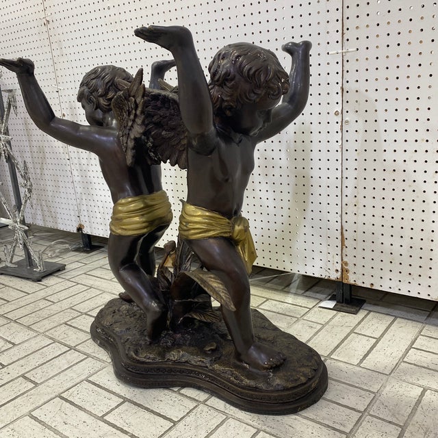 A figural bronze table with a glass top supported by 2 winged putti standing on fantasy inspired naturalistic base....