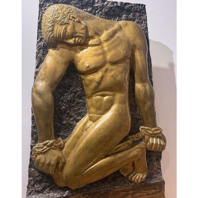 Bold and monumental, this striking relief depicts the mythological figure Prometheus Bound, shown nude and kneeling with...