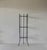 A narrow etagere featuring a matte black metal frame with glass shelves. Circular metal frame with three vertical supports...