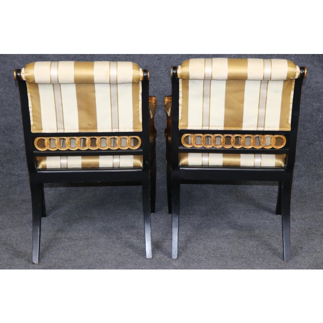 This distinguished pair of Regency-style lion terminal armchairs, executed in dramatic ebonized wood with richly gilded...
