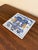 A classic Dutch Delft-style hand painted blue and white porcelain tile featuring an intricately rendered heraldic coat of...