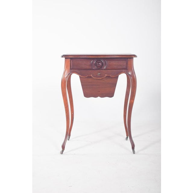 Rosewood potty table. with sharply curved feet, ending in small metal wheels. The top is cut at the ends, with a wavy...