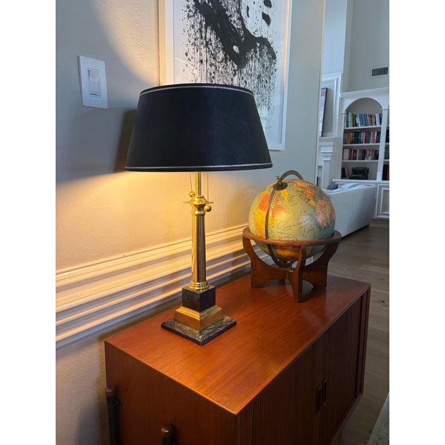 A striking vintage table lamp with a polished brass-tone column rising from a stepped square base of black stone and...