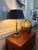 A striking vintage table lamp with a polished brass-tone column rising from a stepped square base of black stone and...