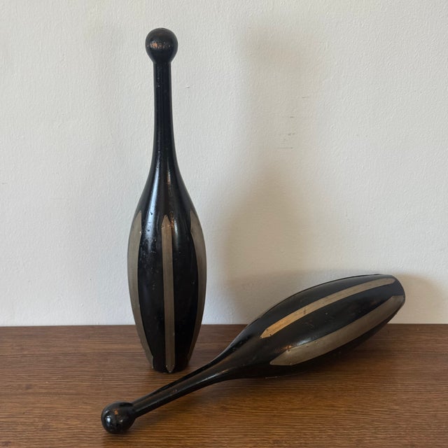 Pair of vintage sculptural turned wood clubs featuring an elongated form with contrasting brass inlay details. Their...