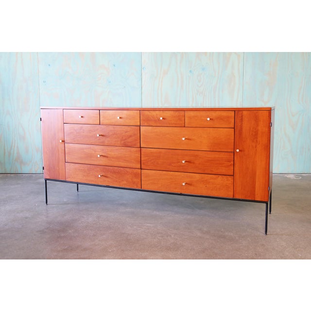 A 1950s highly coveted 20 drawer dresser by Paul McCobb, featuring a black painted iron base that taper to adjustable...