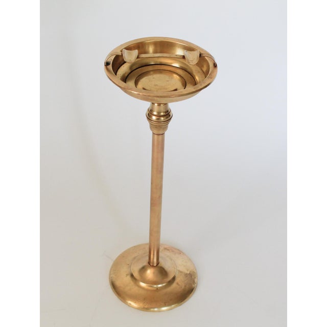 Vintage freestanding brass floor ashtray featuring a slender stem, a central node detail, and a round circular weighted...
