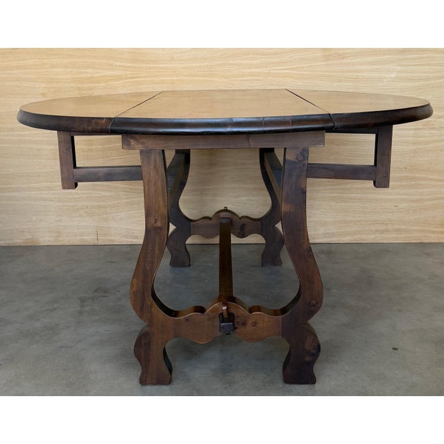 A rustic Spanish walnut drop-leaf table from the 20th century with round top, lyre legs and low stretchers . Embrace the...