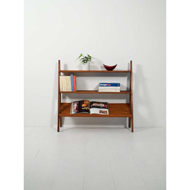 Inverted V-shaped side structure with exposed screws, three teak shelves; the top one is inclined for display. Simple,...