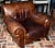 A vintage brown leather club chair featuring rolled arms and noticeable natural distressing and creasing on the leather....