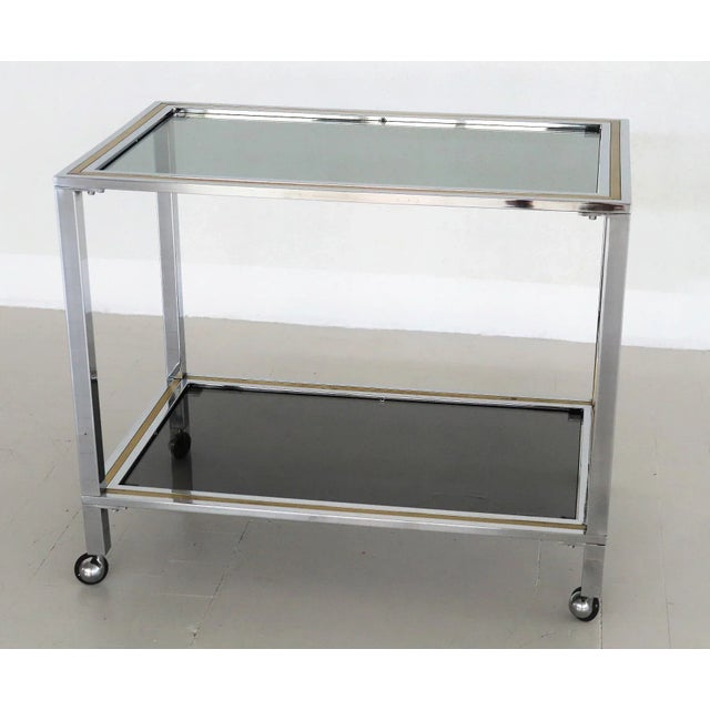 Beautiful bar cart or trolley made in Italy in the 1970s. The trolley is made of shiny chrome and brass and has two smoked...