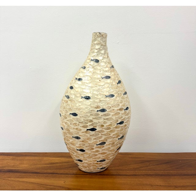 A tall decorative vase featuring an elongated tapered silhouette covered in intricate fish-shaped inlay. Hundreds of...