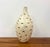 A tall decorative vase featuring an elongated tapered silhouette covered in intricate fish-shaped inlay. Hundreds of...
