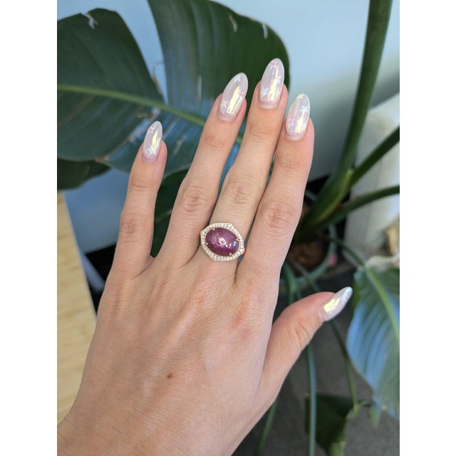 A dramatic star ruby cabochon glows deep red beneath a shimmering halo of diamonds, set in warm solid 14K rose gold. Its...