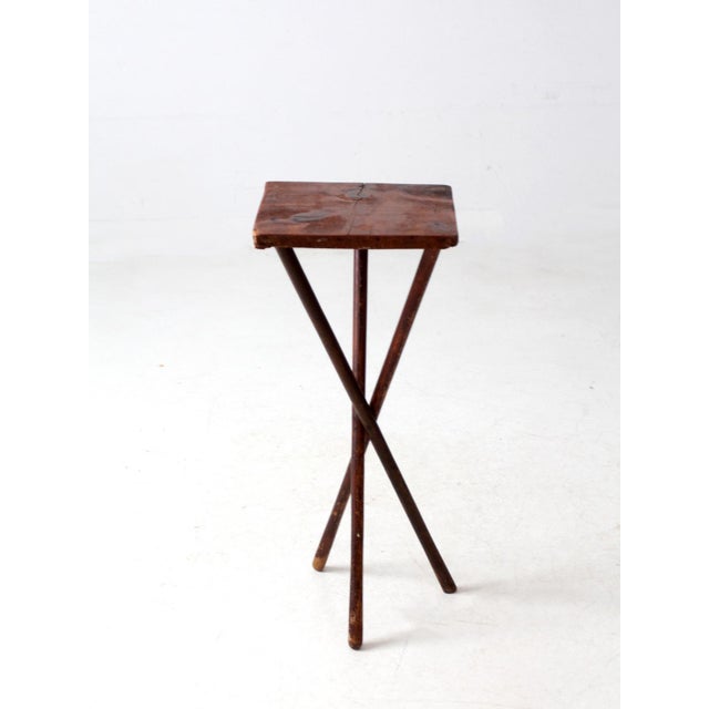 This antique rustic pine side table features a folk art design with three splayed, crossing legs and a simple square top....