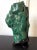 A large malachite rock specimen with intense green and black colors fitted on a wood stand and displayed as a Chinese...