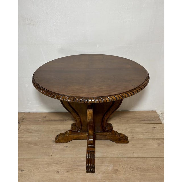 Elegant round side table crafted in richly figured walnut, featuring a sculptural pedestal base with flowing scroll...