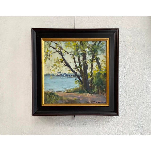 This oil painting captures a tranquil riverside scene bathed in soft, golden light, evoking a sense of peace and serenity....