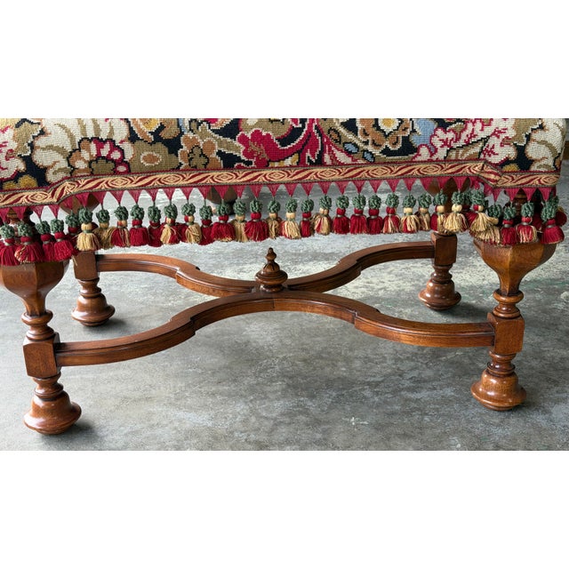 An elegant vintage English Jacobean-style upholstered bench featuring a richly carved walnut frame with beautifully turned...