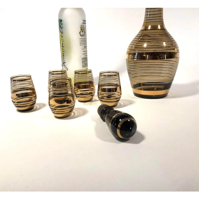 Stunning vintage Bohemian lidded carafe and five shot glass set with 22k gold bands on black and amber glass. So chic!...